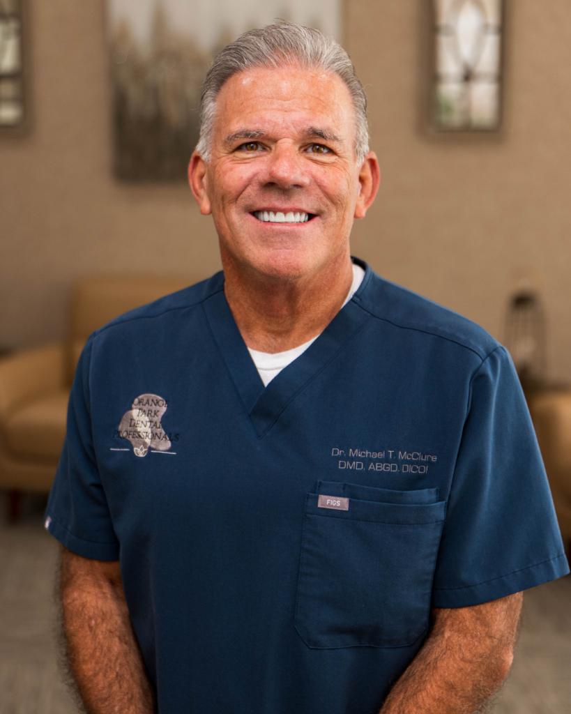 Dr. Michael McClure, an Orange Park dentist, smiling in navy scrubs with the Orange Park Dental Professionals logo in the office seating area 